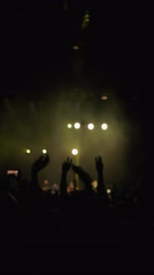 Music Light Show Dark Silhouette of Raised Hands of Fans in Wave Motion Blue and Ellow Strobe Light