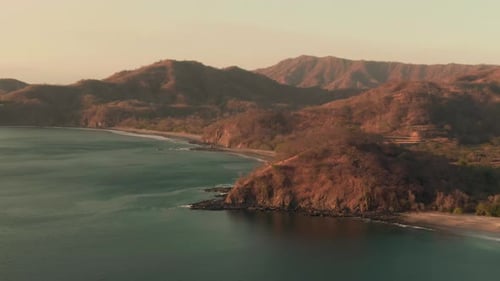 Aerial flight above rocky coastline and beach in Costa Rica sunset