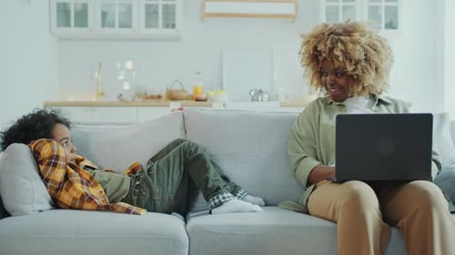 African American Mom Using Laptop and Talking to Little Son at Home