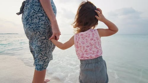Mother and daughter walk on the beach in tropics