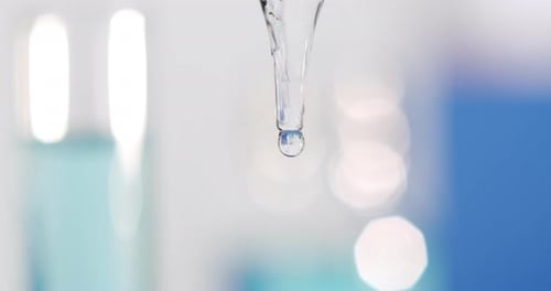 A drop stretching while flowing very slowly from a pipette turned towards the ground, close shot
