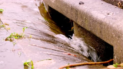 Rainwater runs down concrete gutter into road drain, global warming concept
