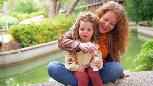 Mother and Cute Girl Blowing Soap Bubbles on a Park