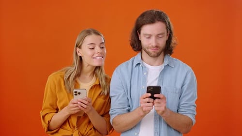 Lady and Guy Spy on Each Other Smartphones in Orange Studio