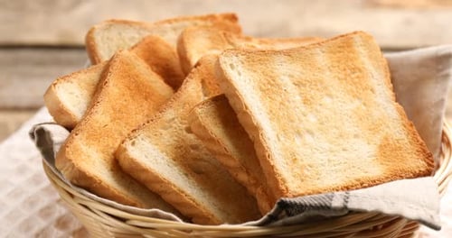 Gebräunte Toastbrotscheiben im Weidenkorb auf Holztisch, Nahaufnahme