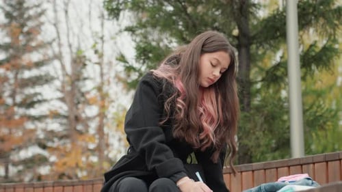 Teenage Girl Sitting Outdoors and Writing on Bench