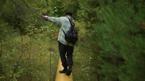 Traveler Balances on Slender Wooden Pathway Quiet Nature Scene Through Thick Green Foliage Corridor