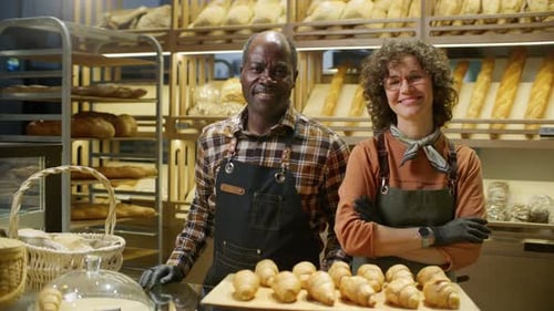 Portrait of Two Happy Bakery Workers Posing with Tray of Fresh Croissants