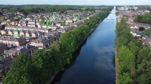 Green arrow icon flashing above sunny British homes alongside long canal, Rising aerial view