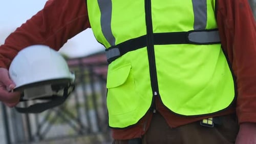 Foreman close-up in a green construction worker's protective vest holding a white helmet in his hand