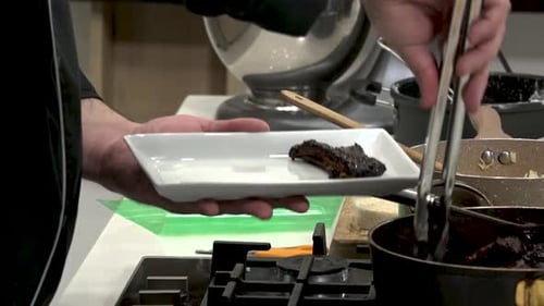 In a contemporary kitchen, a chef skillfully serves a rich dessert from a pot onto a sleek plate, sh