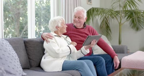Happy Senior Couple Using Tablet on Couch at Home