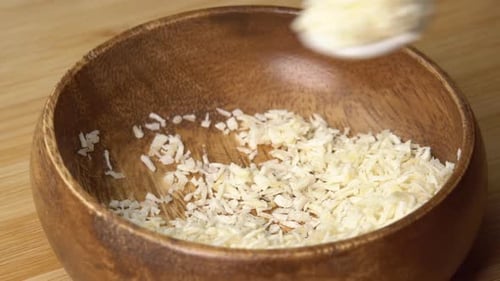 Der
Löffel nimmt Kokosflocken aus einer Holzschale auf und dreht sie auf einem Holzbrett. Kokosraspeln