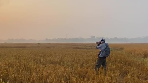 Wide shot of man wearing winter clothes taking pictures with camera of harvest field