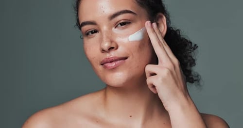 Woman, face cream and happy for skincare in studio on gray background for acne treatment
