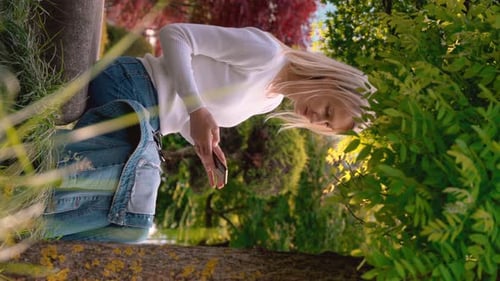Young woman sitting in meadow in park and looking at her phone