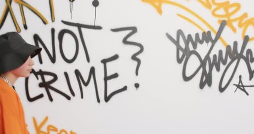 Cool Youngster Walks Pass Graffiti Wall Moves Actively Dressed In Orange T Shirt Trendy Black Hat...