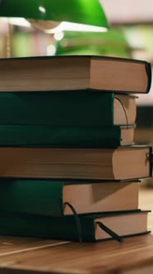 Vertical Video Close Up Green Books in Piles Placed on Table Desk in Library Under Green Lamps