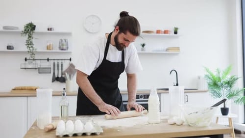 Bearded Man Rolling Dough in Bright Kitchen