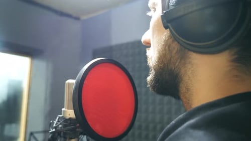 Male Singer with Beard in Headphones Singing Song Into the Microphone at Sound Studio Young Man