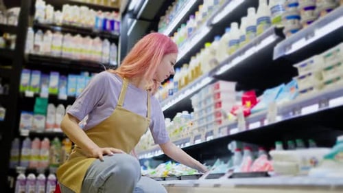Side View of a Confident Girl with Pink Hair Working in a Supermarket and Placing Goods on the Dairy