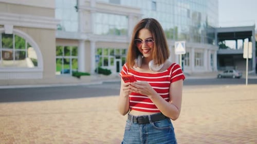 Beautiful Young Woman Uses a Smartphone on the Street Portrait of a Beautiful Girl with Headphones