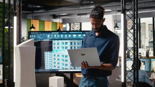 Architect with Laptop Reviews Building Model in Office