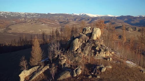 Panoramic shot of a tree-covered rock formation on top of a hill in a dry and mountainous