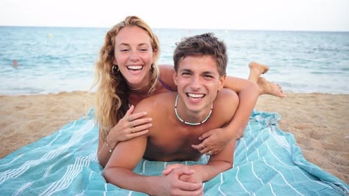 Joyful Couple Enjoying a Sunny Day at the Beach While Lying on a Soft Towel Near the Sparkling Sea