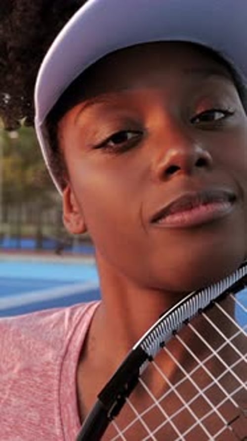 Young black woman tennis player standing confidently on blue court with racket, displaying determina