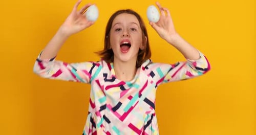 Happy playful teenager girl holding painted Easter eggs covering eyes