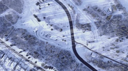 Birds eye view aerial drop in height in a winter town with light traffic and a park next to a highwa