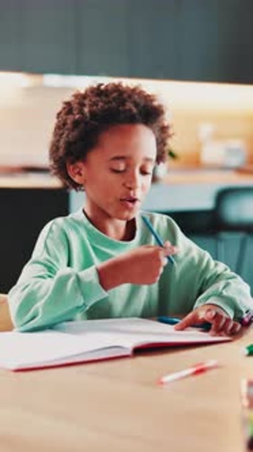 Boy Drawing in Notebook at Table Indoors