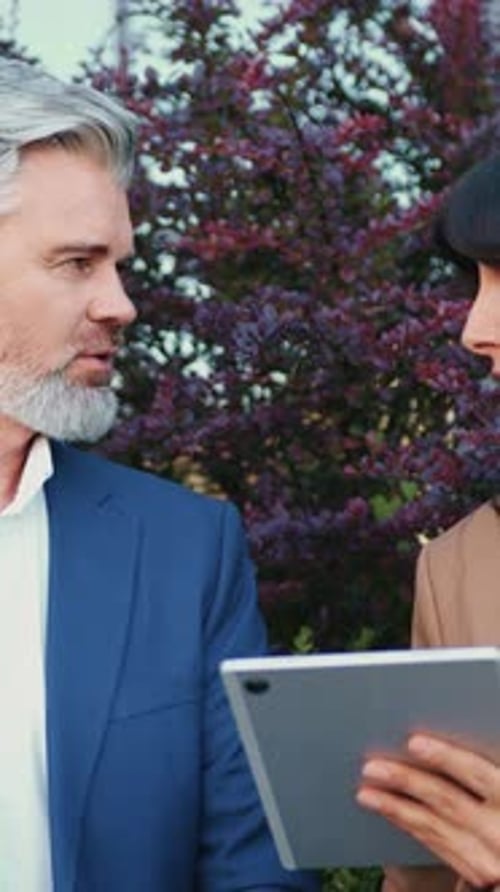 Junge Geschäftsfrau, die ein Tablet in der Hand hält, und ein älterer Geschäftspartner schauen beide auf den Bildschirm, um