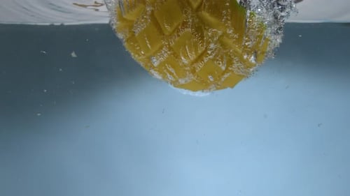 Mango falling into water in super slow motion with blue background. Mango hitting water surface