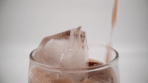 Pouring cola into a glass with ice close up isolated