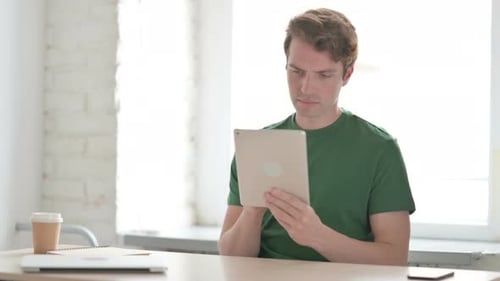 Young Adult Man Using Tablet at Desk