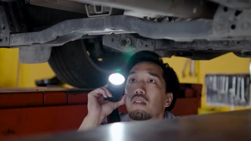 Young Adult Mechanic Inspecting Car Underside with Flashlight