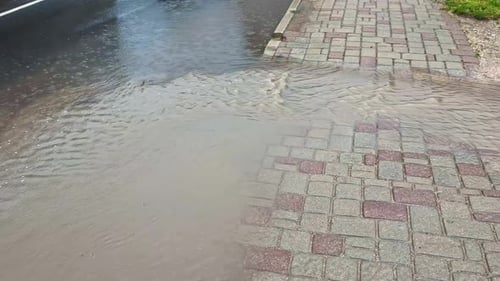 Rainwater overflowing onto a paved sidewalk as runoff from the street creates shallow flooding