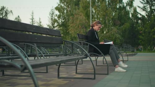 Businesswoman Reading Documents on Park Bench with Laptop in Peaceful Outdoor Setting