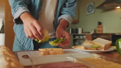 Close-up of hands of young man cooking sandwich standing in the kitchen