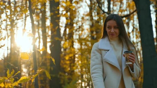 Woman Walking in Autumn Park with Coffee