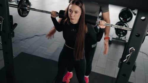 Woman Doing Barbell Squats With Personal Trainer at the Gym