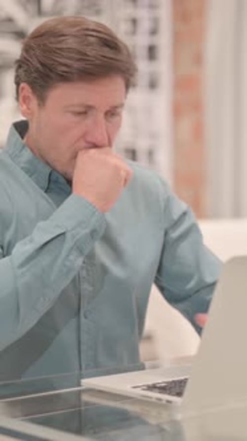 Man Coughing While Working at Laptop Indoors