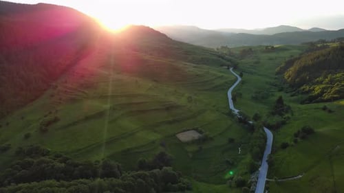 A Road Passes Hills Covered with Spruce Forests and Meadows Against a Cloudy Sky