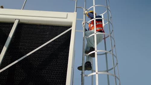 Professional technician climbs a caged metal ladder to inspect an industrial cooling tower rooftop