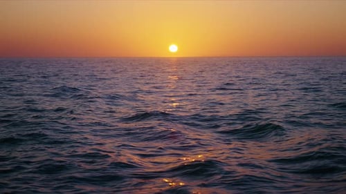 Ein ruhiger Sonnenuntergang, der in Zeitlupe warme Farben über sanfte Meereswellen wirft