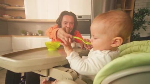Man Feeding Cute Baby in Highchair at Home