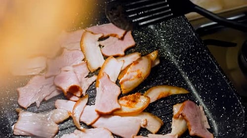 The Cook Stirs the Frying Bacon with a Spoon