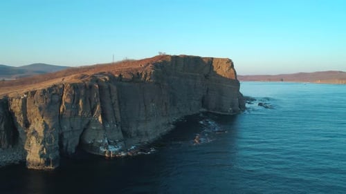 Aerial Drone View of an Ocean Blue Waves Break on High Cliff of a Rocky Mountain During the Sunset